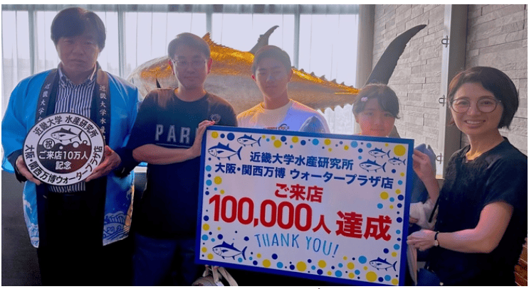近畿大学水産研究所　大阪・関西万博ウォータープラザ店　来店者10万人達成セレモニーを開催　記念スタンプを設置
